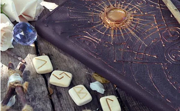 Un carnet de cuir gravé et des runes claires posées sur une table en bois
