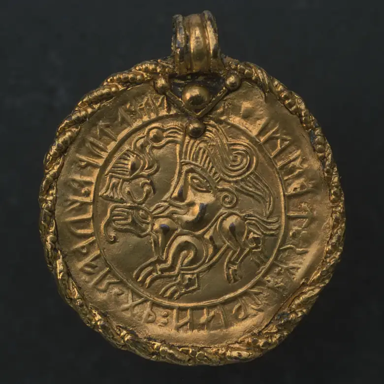 La bractéate de Vadstena : un médaillon d’or à bélière, orné d’une tête humaine au-dessus d’un animal et entouré d’une inscription runique.